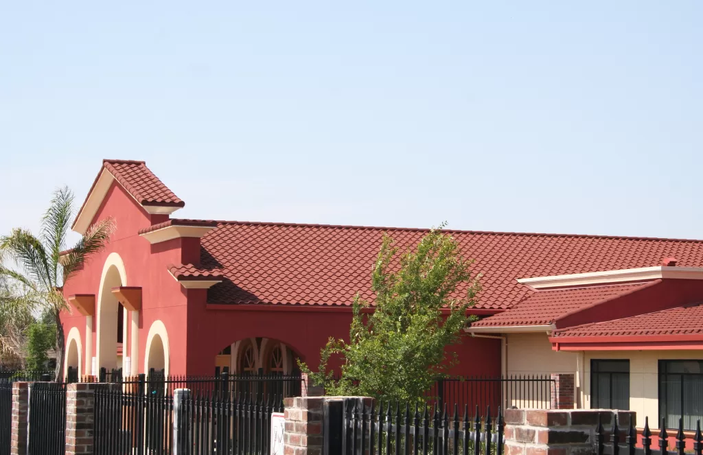 A bright, terra-cotta-colored clay tile roof on a building with arches and a palm tree in the foreground, showcasing southwestern architecture.